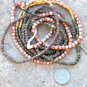 May include: A close-up of a pile of vintage glass beads. The beads are in three colors: brown with yellow stripes, white with orange stripes, and orange with white stripes.