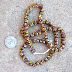 May include: A strand of brown, white, and yellow striped glass beads. The beads are round and have a slightly irregular shape. The beads are strung on a white cord.