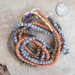 May include: A collection of vintage glass beads in orange, black, and white. The beads are strung together in a variety of patterns, creating a unique and colorful necklace.