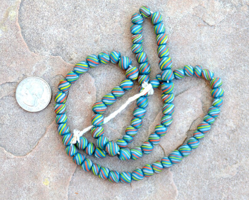 May include: A strand of blue, green, white and orange glass beads. The beads are round and have a swirl pattern. The beads are about the size of a UK 20 pence coin.