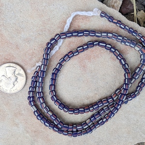 May include: A strand of blue, white, and orange glass beads. The beads are cylindrical and have a striped pattern. The beads are about the size of a US quarter.