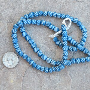 May include: A strand of blue and white glass beads. The beads are round and have a swirl pattern. The beads are strung on a white cord.