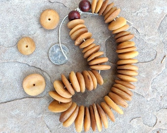 May include: A strand of wooden beads in shades of brown, beige, and tan. The beads are round and flat, and they are strung together on a white cord. There are also several smaller, round wooden beads in the image.