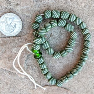 May include: A strand of green and white striped beads with a green glass bead accent. The beads are strung on a white cord.