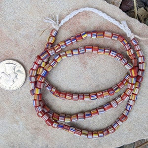 May include: A strand of colorful glass beads with red, white, blue, and yellow stripes. The beads are strung on a white cord and are arranged in a circular pattern.