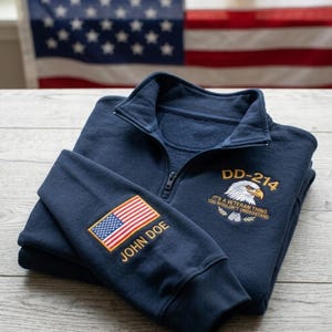 Puede incluir: Sudadera azul marino con cremallera de cuarto de cremallera y detalles bordados. Presenta un parche de la bandera estadounidense y el nombre "JOHN DOE" en la manga. El pecho muestra "DD-214" y un diseño de águila patriótica con el texto "IT'S A VETERAN THING YOU WOULDN'T UNDERSTAND."