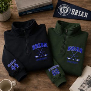 May include: Two quarter-zip pullovers, one black and one green, with embroidered "Briar University" logos and hockey stick graphics. The black pullover has "Graham 44" on the sleeve, and the green one has "St Laurentis 66".
