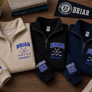 May include: Three quarter-zip sweatshirts in beige, black, and navy blue, each embroidered with "Briar University" and crossed hockey sticks. Sleeves display names and numbers. A navy pennant with "Briar" and a logo is also visible.