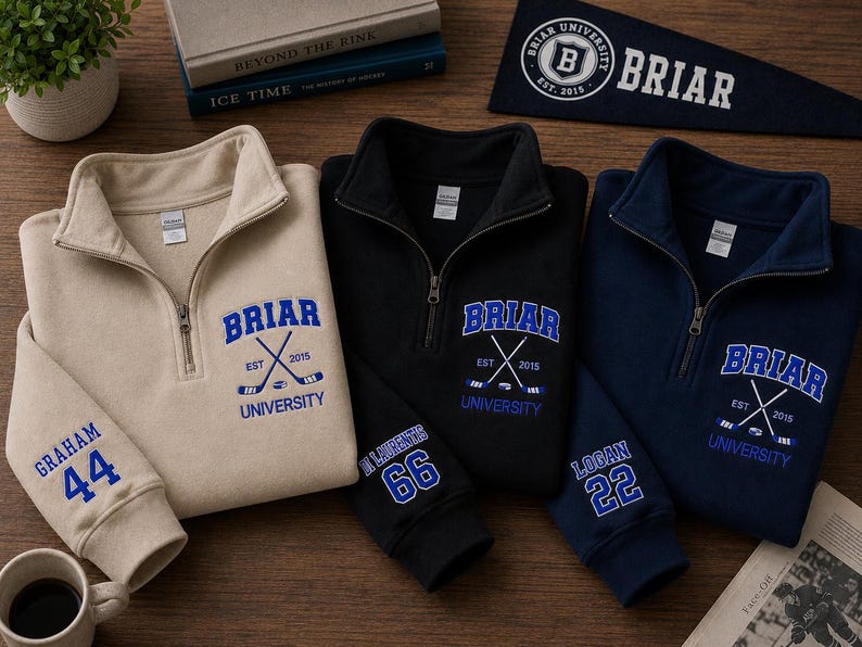 May include: Three quarter-zip sweatshirts in beige, black, and navy blue, each embroidered with "Briar University" and crossed hockey sticks. Sleeves display names and numbers. A navy pennant with "Briar" and a logo is also visible.