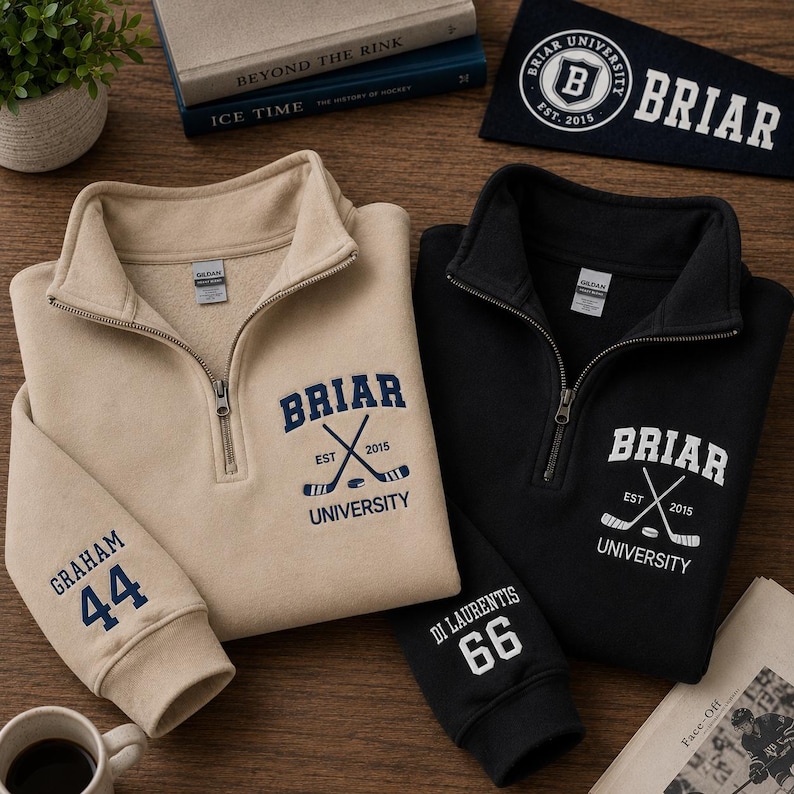 May include: Two quarter-zip sweatshirts, one tan and one black, with the text "BRIAR UNIVERSITY" and crossed hockey sticks. The tan sweatshirt has "GRAHAM 44" on the sleeve, while the black one has "DI LAURENTIS 66". A pennant and books are in the background.