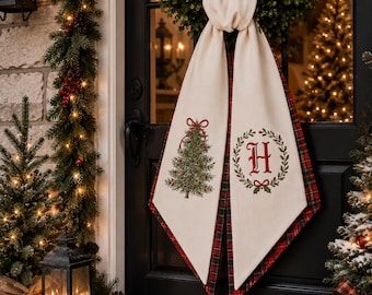 May include: A cream-colored fabric door hanger draped over a green wreath, featuring a red and green plaid backing. The left panel displays a decorated Christmas tree with a red bow, while the right panel shows a red letter H inside a green wreath.