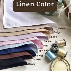 May include: A stack of linen fabric swatches in white, beige, sand, purple, pink, light blue, navy, brown, and black. The text Linen Color is at the top. Several spools of thread in light blue, beige, and black are positioned next to the fabric.