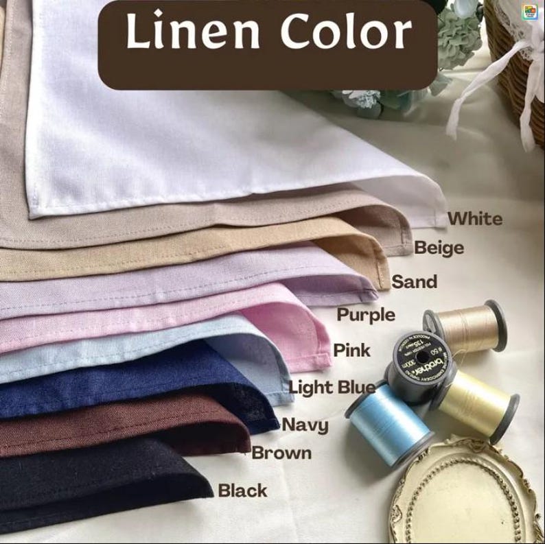 May include: A stack of linen fabric swatches in white, beige, sand, purple, pink, light blue, navy, brown, and black. The text Linen Color is at the top. Several spools of thread in light blue, beige, and black are positioned next to the fabric.