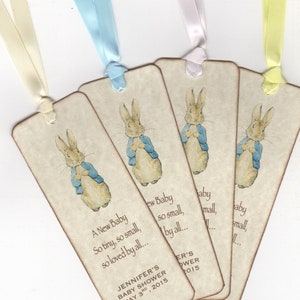 May include: Four beige bookmarks with a picture of Peter Rabbit on each. The bookmarks have a ribbon attached to the top. The text on the bookmarks reads "A New Baby So tiny, so small, so loved by all... Jennifer's Baby Shower May 3rd, 2015".