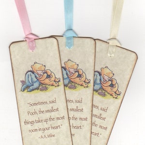 K&ouml;nnte beinhalten: Drei Winnie-the-Pooh-gebundene Lesezeichen mit einem Zitat von A.A. Milne. Die Lesezeichen sind beige mit einem braunen Band, das oben befestigt ist. Das Zitat lautet: "Manchmal, sagte Winnie, nehmen die kleinsten Dinge den meisten Platz in deinem Herzen ein." - A.A. Milne. Die Lesezeichen enthalten auch den Text "Rachel's Baby Shower September 29, 2018".