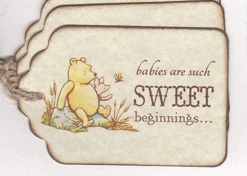 May include: A Winnie the Pooh themed baby shower favor tag with a brown background and a picture of Winnie the Pooh and Piglet. The text on the tag reads "babies are such SWEET beginnings..."