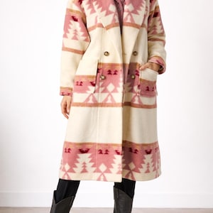 Puede incluir: Abrigo largo color crema con diseño de doble botonadura. El abrigo presenta un estampado geométrico en tonos rosas y marrones. Tiene dos bolsillos delanteros y se lleva con botas negras.