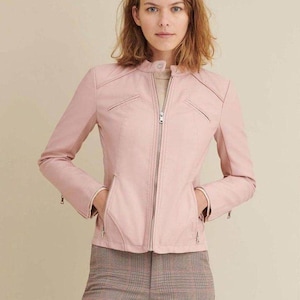 Puede incluir: Chaqueta rosa claro con cuello alzado y cremallera plateada. La chaqueta tiene dos bolsillos delanteros y un corte entallado. Las mangas tienen cremalleras en los puños. La modelo lleva un top beige y pantalones a cuadros.