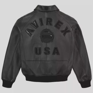 K&ouml;nnte beinhalten: Schwarze Leder-Bomberjacke mit Kragen und gerippten B&uuml;ndchen. Auf der R&uuml;ckseite steht der Text "AVIREX USA" in erhabenen, schwarzen Buchstaben. Ein kreisf&ouml;rmiges Emblem ist &uuml;ber dem Text zentriert. Die Jacke hat ein klassisches, zeitloses Design.
