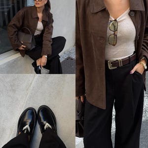 May include: A brown suede jacket, paired with black trousers and black loafers. The outfit includes a beige top, a brown leather belt, and a dark brown handbag. The loafers have a silver accent.