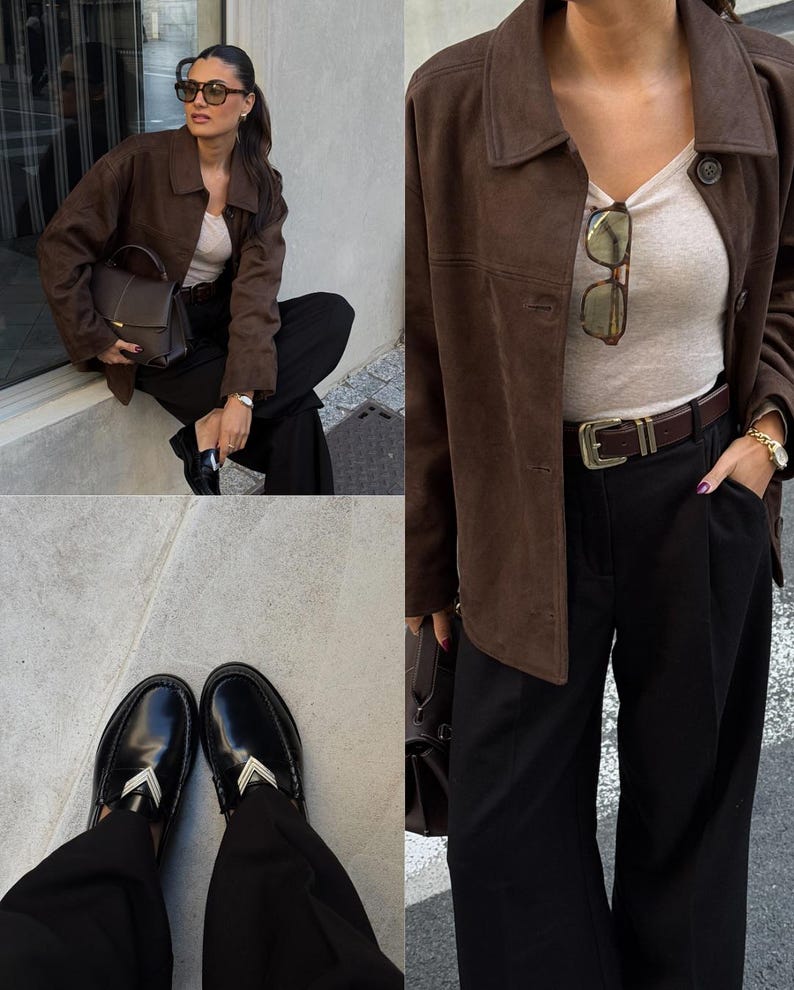 May include: A brown suede jacket, paired with black trousers and black loafers. The outfit includes a beige top, a brown leather belt, and a dark brown handbag. The loafers have a silver accent.