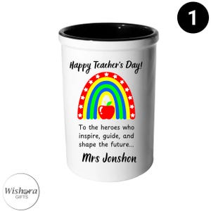 Könnte beinhalten: Weißer Keramik-Stifthalter mit schwarzem Rand, mit Regenbogen- und Apfeldesign. Der Text lautet "Happy Teacher's Day!" und "To the heroes who inspire, guide, and shape the future... Mrs Jonshon."