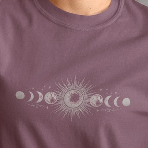 Op de afbeelding: Mauvekleurig T-shirt met een hemels ontwerp. De afbeelding toont een zon en maanfasen in een lijn over de borst. Het shirt is gemaakt van zacht materiaal en heeft korte mouwen.