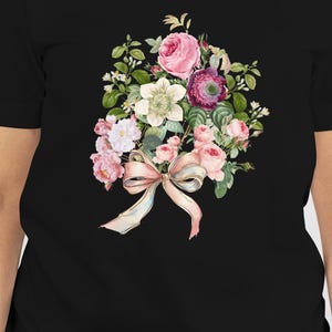 Op de afbeelding: Zwart T-shirt met een aquarel bloemenboeket ontwerp. Het boeket bevat roze rozen, witte bloemen en groene bladeren, vastgebonden met een lichtroze strik. Het T-shirt heeft een klassieke ronde hals.
