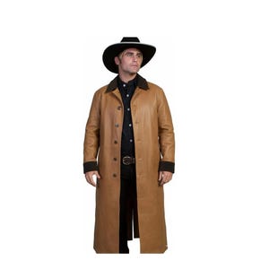 Puede incluir: Un abrigo largo de cuero marrón claro con botones, cuello y puños negros. El abrigo se lleva con una camisa negra, pantalones negros y un sombrero de vaquero negro. Se ve un cinturón marrón con hebilla plateada.