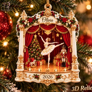 May include: A 3D relief acrylic ornament featuring a stage with red curtains, a ballerina in a white tutu, a nutcracker, a Christmas tree, and gifts. The top is inscribed with the name Olivia and the base displays the year 2026 in gold.