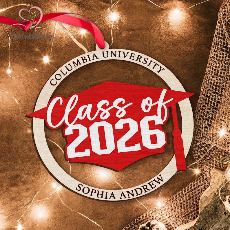 May include: A wooden Columbia University graduation ornament. The ornament features a red mortarboard shape with "Class of 2026" in white script. The name "Sophia Andrew" is below. A red ribbon is attached for hanging.