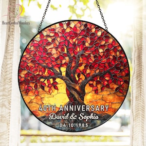 May include: A round stained glass panel featuring a tree with red and orange leaves. The tree's trunk is brown, and the panel includes the text "40TH ANNIVERSARY David & Sophia 04.10.1985". The panel is suspended by a black chain.