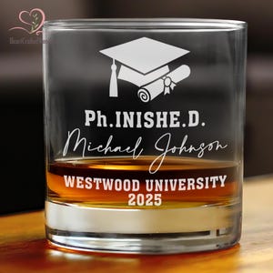 May include: A clear glass with a white graduation cap and diploma design. The text reads "Ph. INISHE. D. Michael Johnson WESTWOOD UNIVERSITY 2025".
