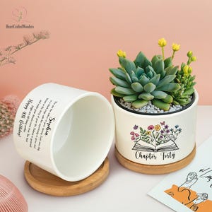 May include: Two white ceramic planters with wooden saucers. One planter is empty, with text that reads "Happy 40th Birthday! Sophia". The other planter contains a succulent plant and has a floral design with the text "Chapter Forty".
