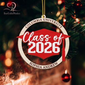 May include: Wooden Columbia University graduation ornament. The ornament features a red graduation cap with the words "Class of 2026" in white. The name "Sophia Andrew" is below the cap. The words "Columbia University" are in a circle around the cap.
