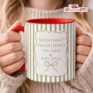May include: A ceramic mug with a red handle and interior, featuring a white and gold vertical striped pattern. The front displays a decorative frame containing the text: NEVER FORGET THE DIFFERENCE YOU MAKE, a small heart, MRS. EMILY, and a bow.