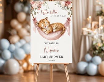 May include: A baby shower sign on a wooden easel. The sign features a watercolour illustration of a sleeping orange tabby kitten in a pink hammock. Text includes "a little kitten is on the way," "Welcome to Nedrah's," and "Baby Shower."