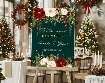 May include: A vertical rectangular wedding sign with a dark green background featuring floral illustrations of red poinsettias, white roses, pine cones, and greenery. The text reads: Tis the season TO BE MARRIED, Amanda & Steven, DECEMBER 20, 20XX.