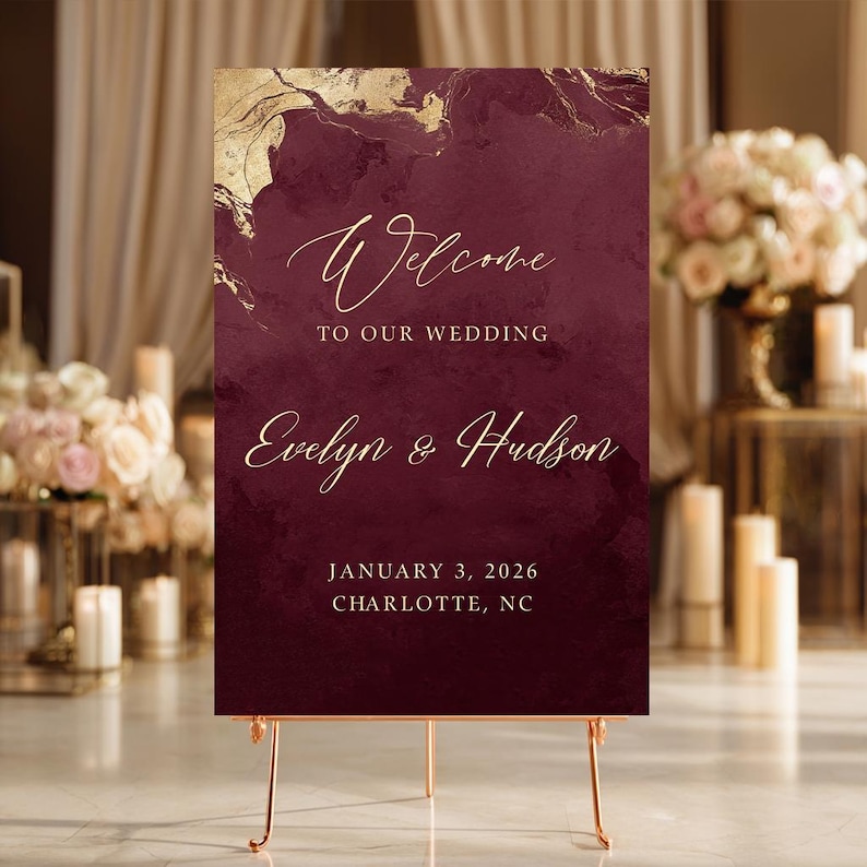 May include: A rectangular wedding welcome sign featuring a deep burgundy background with gold marble-like accents at the top. The text reads: Welcome TO OUR WEDDING Evelyn & Hudson JANUARY 3, 2026 CHARLOTTE, NC in elegant gold script and block lettering.