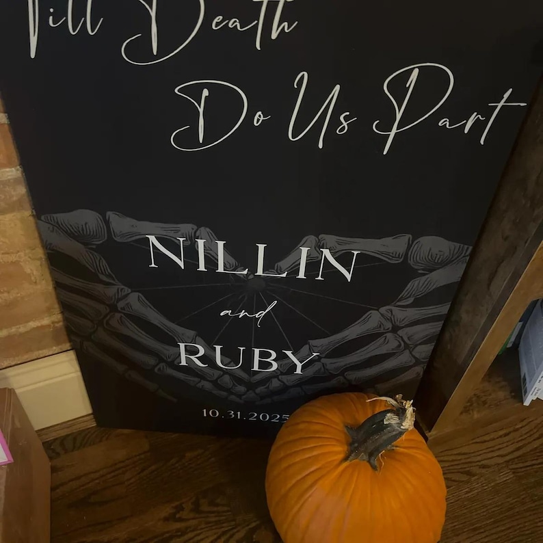 May include: A black rectangular sign featuring the white text Till Death Do Us Part, NILLIN and RUBY, and 10.31.2025. The design includes a graphic of two skeletal hands forming a heart shape. An orange pumpkin sits in front of the sign.