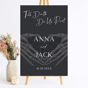 May include: A rectangular dark gray wedding sign on a wooden easel featuring the white text Till Death Do Us Part, the names Anna and Jack, and the date 10.20.20XX. The design includes a graphic of two skeletal hands forming a heart shape.