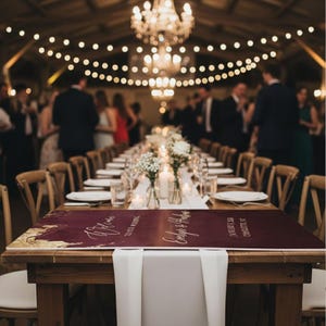 May include: A rectangular wedding welcome sign in deep burgundy with gold accents, featuring white cursive text that reads Welcome to our wedding, Evelyn & Hudson, January 7, 2023, Charlotte, NC, placed on a wooden table with a white runner.