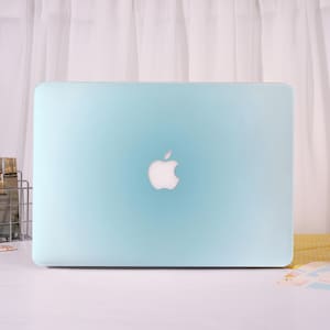 May include: A light blue laptop cover featuring a smooth, matte finish and a central cutout that reveals the white Apple logo. The protective shell is designed to fit the rectangular shape of the device, providing a solid, uniform color across the surface.