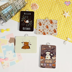 Könnte beinhalten: Eine Sammlung von Kartenhaltern mit verschiedenen Designs. Ein Kartenhalter ist schwarz mit dem Text "Hello October" und einer Mond- und Geistergrafik. Andere Kartenhalter zeigen Kürbisse, Geister und einen Teddybären. Ein "Happy Halloween"-Kartenhalter zeigt einen Geisterkoch.