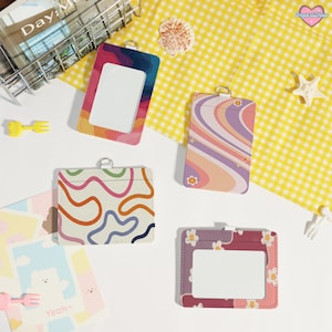 May include: Four colorful ID badge holders with various designs, including a rainbow, wavy lines, and floral patterns. Each holder has a clear window for displaying an ID and a silver ring for attaching a lanyard.