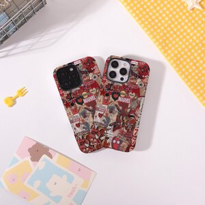 May include: Two phone cases with a collage design featuring Spider-Man and Marvel logos. The cases are primarily red with a variety of images and text. The cases are on a white surface with a yellow fork and a small notepad.