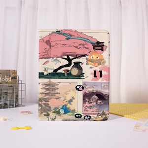 May include: A rectangular notebook featuring a collage of Japanese-inspired illustrations. The design includes a pink cherry blossom tree, a pagoda, and various animated characters. The word "青" is visible in the upper right corner, and the number "L1" is also present.