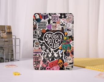 May include: A black Kindle case covered in stickers with a spooky theme. The stickers include images of skulls, ghosts, pumpkins, and text that reads "Spooky Bitch Club", "Coffee & Horror Movies", and "Kindle Girlie".