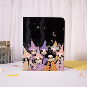 May include: A rectangular notebook featuring a dark night sky illustration with a crescent moon and a group of stylised figures wearing pointed hats and ruffled collars in shades of pink, purple, yellow, and orange against a black background.