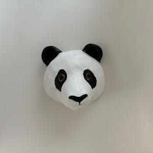 May include: A white panda face mask with black ears and eyes. The mask has a black nose and mouth.